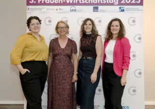 Vier Frauen stehen lächelnd vor dem Banner des dritten Frauen-Wirtschaftstags 2025
