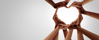 Mehrere Hände formen ein Herz. Sie symbolisieren Zusammenhalt, Liebe und Gemeinschaft vor einem grauen Hintergrund.