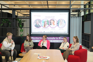 Auf dem Bild sehen wir eine Diskussionsrunde mit mehreren Frauen, die über Mentoring und Feminisierung sprechen. Der Fokus liegt auf Interviews und Austausch.