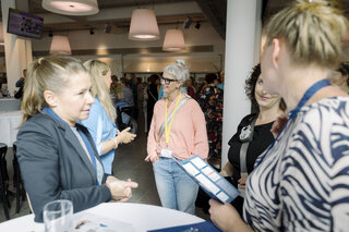 Das Bild zeigt eine Gruppe von Menschen in einem modernen Veranstaltungsraum, die sich in einem Gespräch austauschen. Einige Personen lächeln.