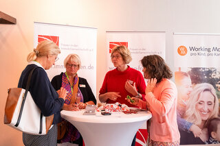 In einem Event-Raum stehen vier Frauen am Messestand. Sie diskutieren angeregt und tauschen Informationen über die Immobilienwirtschaft aus.