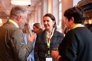 Das Bild zeigt eine Gruppe von Menschen, die in einem ansprechenden, hellen Raum miteinander sprechen und sich austauschen. Es herrscht eine freundliche Atmosphäre.