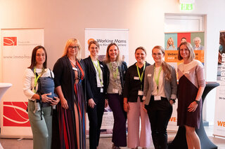 Das Bild zeigt eine Gruppe von Frauen, die an einem Event teilnehmen, lächeln und sich in einer freundlichen Atmosphäre präsentieren.