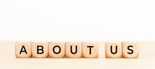 Die Buchstaben auf Holzblöcken bilden den Schriftzug „ABOUT US“ und stehen für Informationen über eine Gruppe oder Organisation.