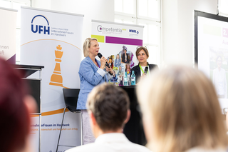 Auf dem Bild sind zwei Frauen zu sehen, die an einem Podiumsgespräch teilnehmen. Im Hintergrund sind Banner von UFH und Competentia zu erkennen.